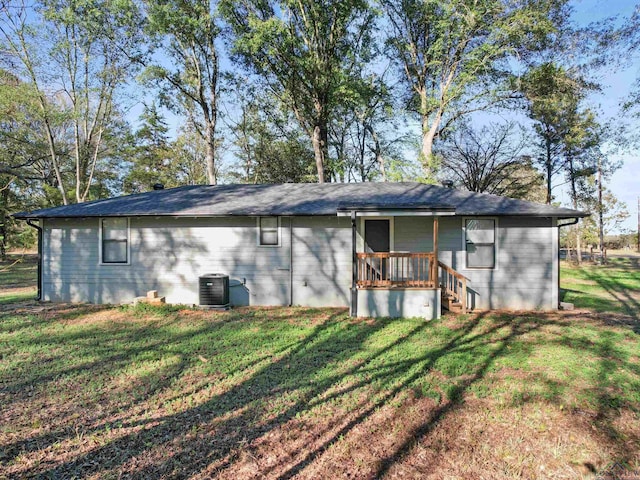 rear view of house with central AC unit and a lawn