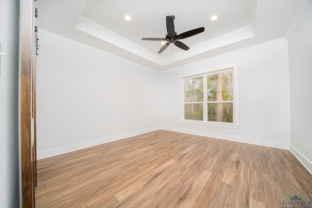 spare room with a raised ceiling, light wood-type flooring, crown molding, and ceiling fan