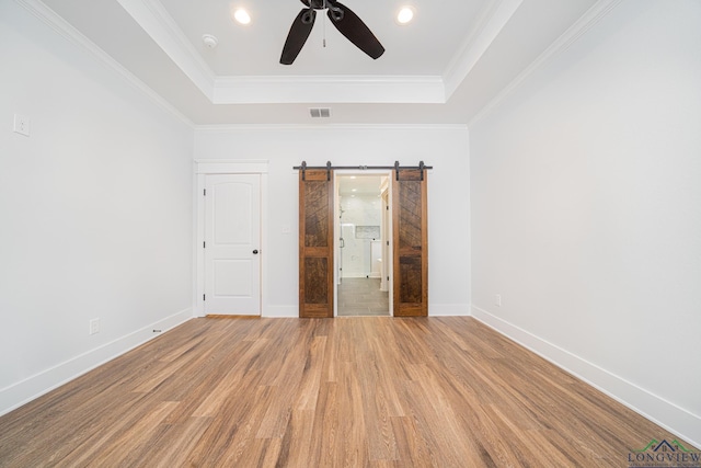 unfurnished bedroom featuring ceiling fan, hardwood / wood-style flooring, a raised ceiling, and a barn door