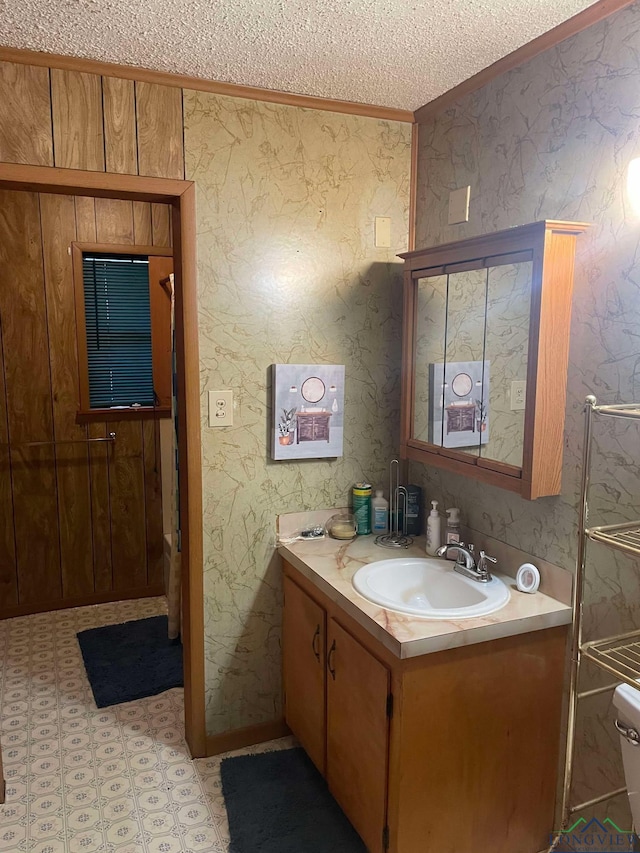 bathroom featuring a textured ceiling, vanity, ornamental molding, tile patterned floors, and wallpapered walls