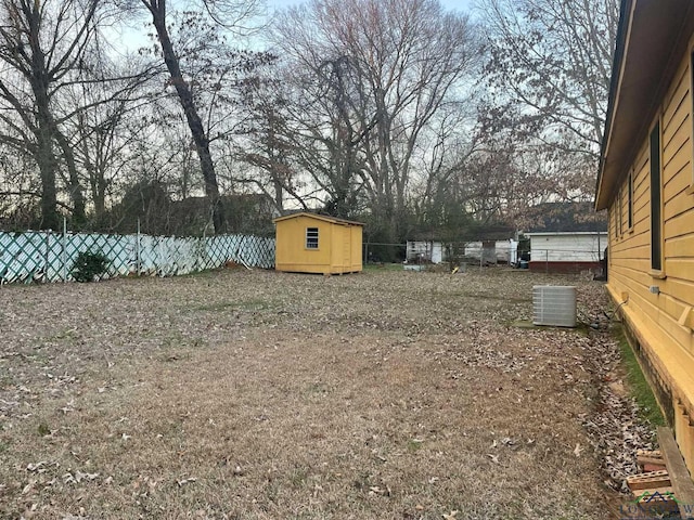 view of yard with a fenced backyard, an outdoor structure, central AC, and a storage shed