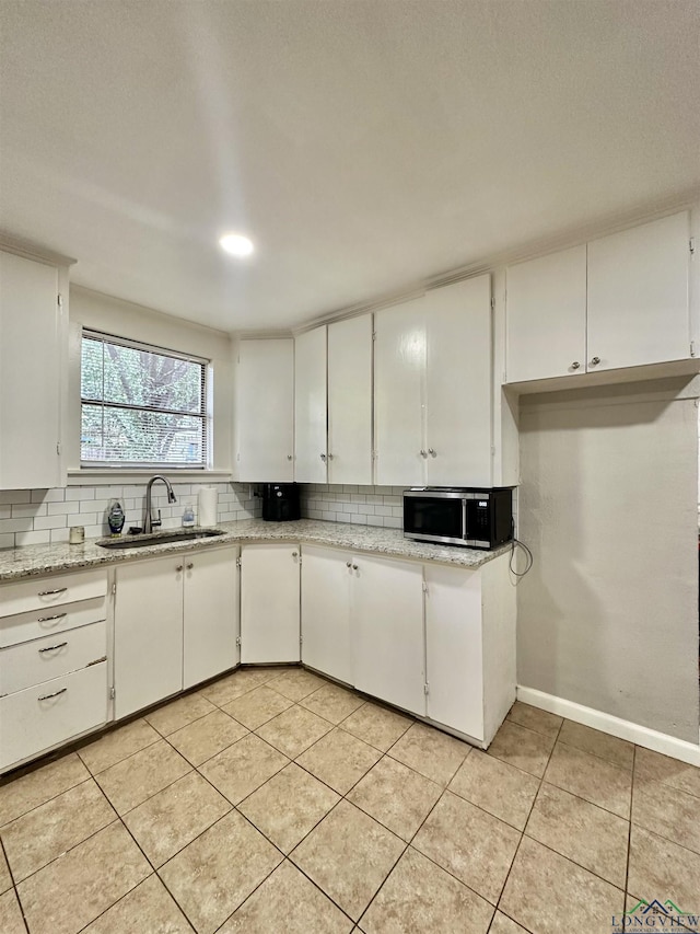 kitchen featuring light tile patterned floors, light stone counters, white cabinetry, and sink