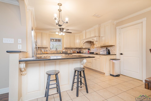 kitchen featuring sink, ornamental molding, light tile patterned floors, ceiling fan with notable chandelier, and a breakfast bar area