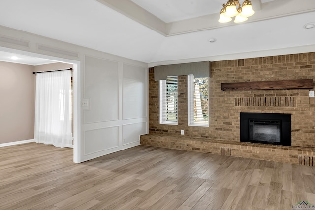 unfurnished living room with light wood-type flooring, a fireplace, and an inviting chandelier