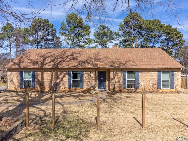 ranch-style house with a front yard, roof with shingles, a chimney, and brick siding