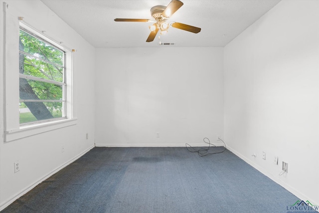 empty room with ceiling fan, visible vents, a wealth of natural light, and dark carpet