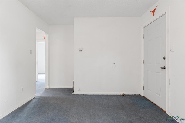spare room with baseboards and dark carpet