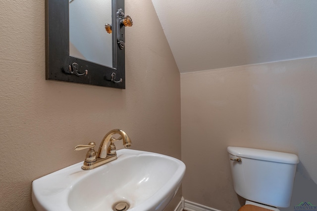 bathroom with toilet, vaulted ceiling, and sink