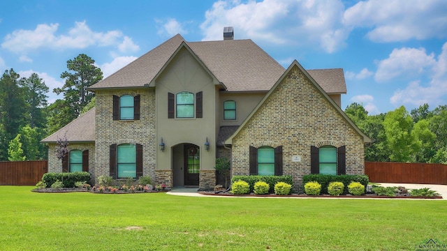 view of front of house featuring a front lawn, fence, brick siding, and stucco siding