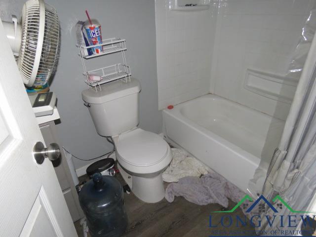 bathroom featuring hardwood / wood-style flooring, shower / bath combination with curtain, and toilet