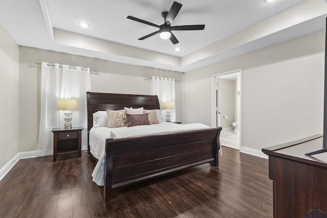 bedroom with dark hardwood / wood-style floors, ceiling fan, a raised ceiling, and ensuite bath