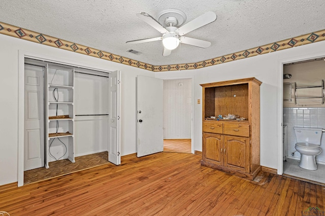 unfurnished bedroom featuring ceiling fan, hardwood / wood-style floors, ensuite bath, and a textured ceiling