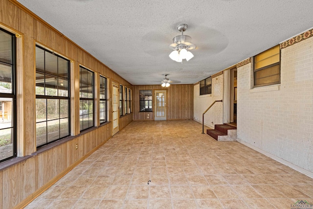 empty room featuring brick wall, wood walls, ceiling fan, and a textured ceiling