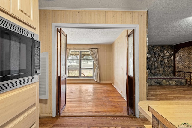 hall with light hardwood / wood-style floors, wood walls, and a textured ceiling