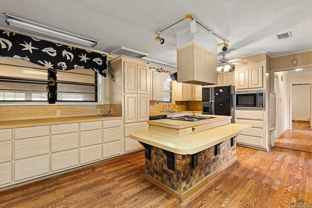 kitchen featuring stainless steel gas cooktop, built in microwave, ceiling fan, a textured ceiling, and black refrigerator with ice dispenser