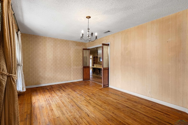 spare room with a textured ceiling, light wood-type flooring, and a chandelier