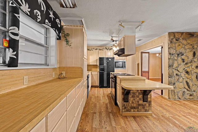 kitchen with wooden walls, a textured ceiling, range with gas cooktop, black fridge, and light brown cabinets