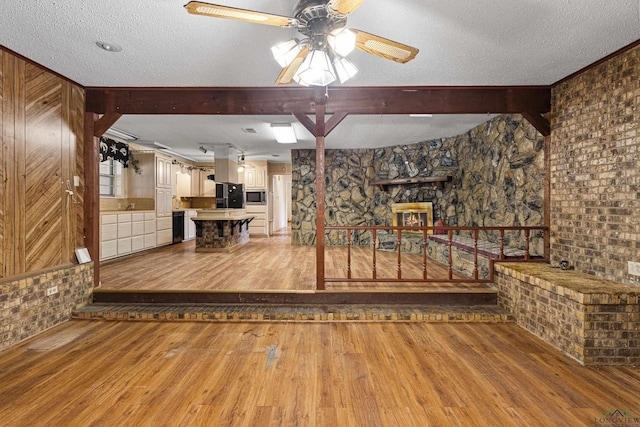 interior space with a textured ceiling, ceiling fan, light hardwood / wood-style flooring, and a stone fireplace