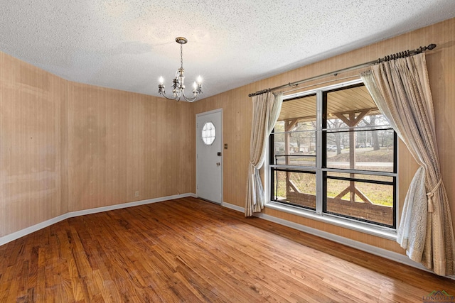 interior space with a healthy amount of sunlight, an inviting chandelier, a textured ceiling, and wood-type flooring