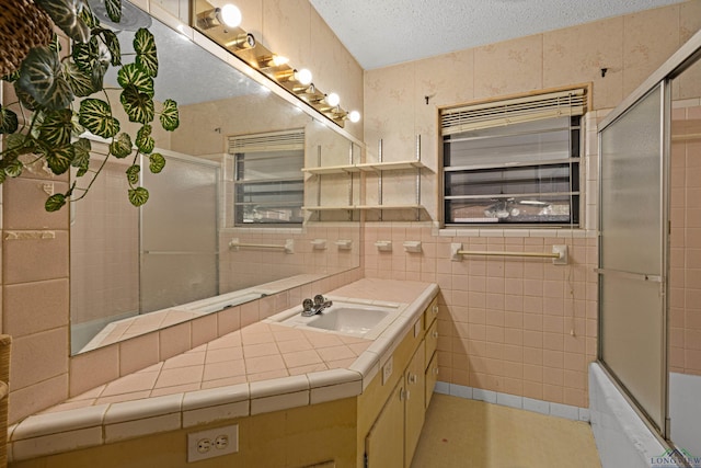 bathroom featuring vanity, tile walls, a textured ceiling, and enclosed tub / shower combo