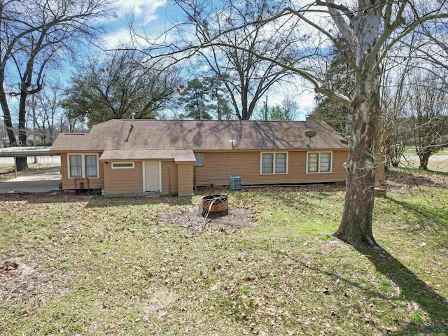 rear view of house featuring central air condition unit, a yard, a fire pit, and a carport