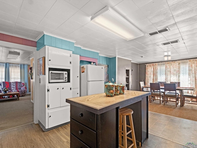 kitchen with a center island, white cabinets, white fridge, dark brown cabinetry, and a breakfast bar area