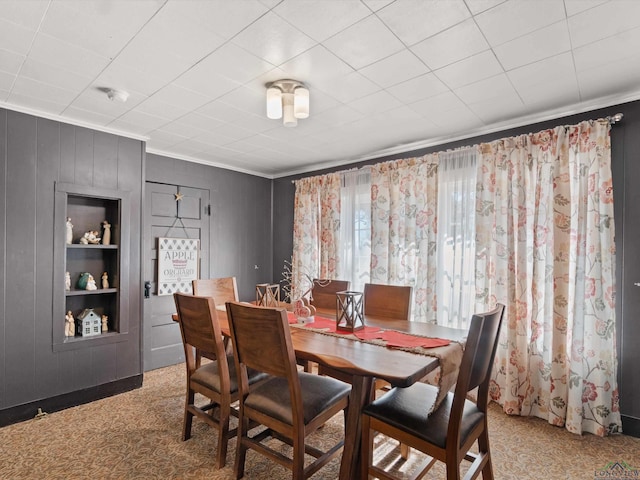 dining room featuring carpet flooring, wooden walls, built in features, and crown molding