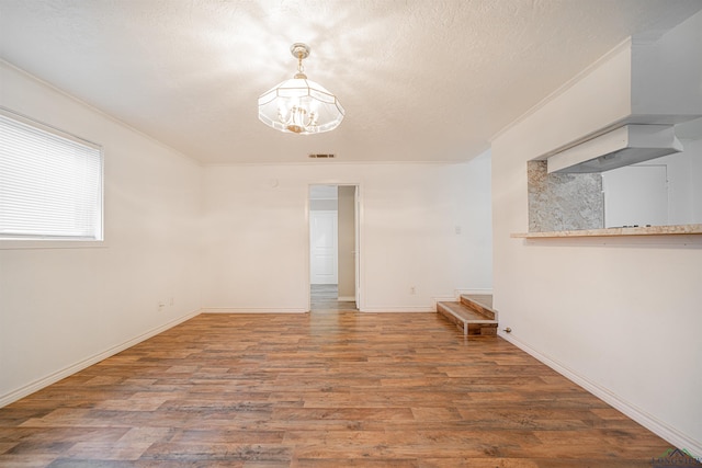 empty room featuring a textured ceiling, crown molding, dark wood-type flooring, and a chandelier