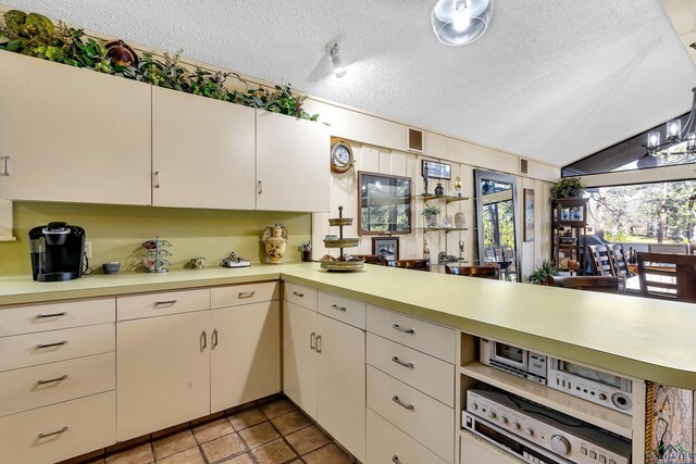 kitchen with lofted ceiling, kitchen peninsula, a textured ceiling, and light tile patterned floors