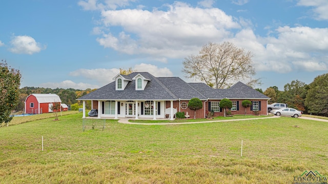 view of front of house featuring covered porch, brick siding, a front yard, and a barn