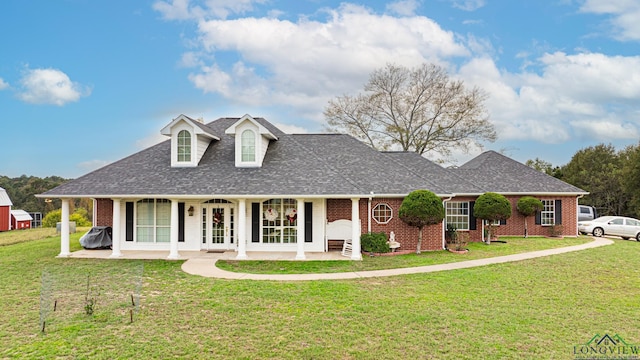 view of front of house with a shingled roof, a front yard, a porch, and brick siding