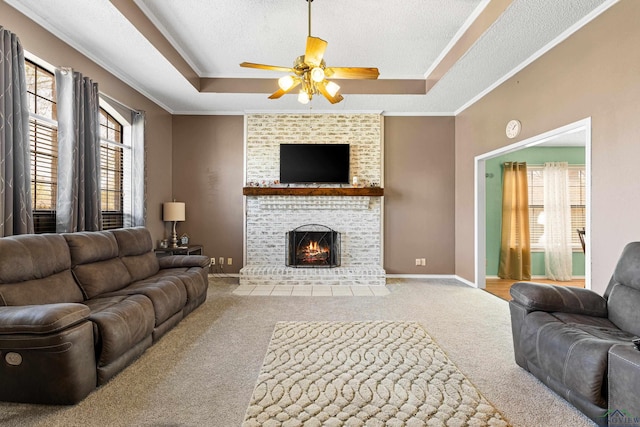 carpeted living room featuring baseboards, a fireplace, ceiling fan, a textured ceiling, and a raised ceiling