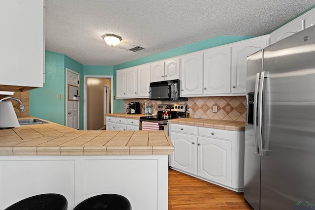kitchen featuring visible vents, a sink, white cabinetry, appliances with stainless steel finishes, and a peninsula