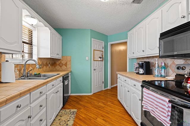 kitchen featuring light wood-style flooring, a sink, white cabinets, black microwave, and stainless steel electric range oven