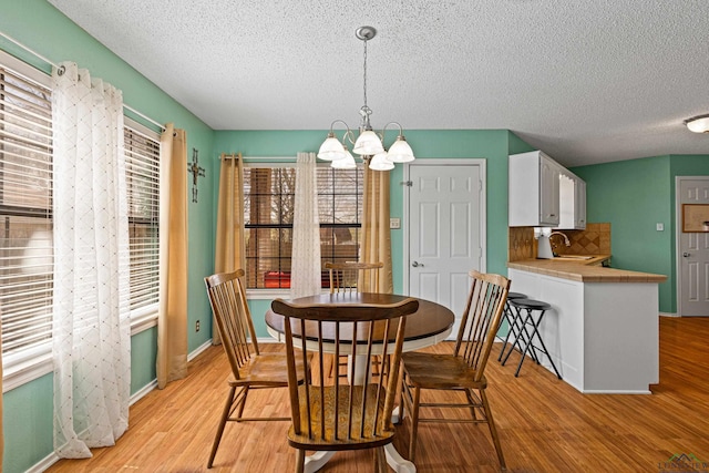 dining space featuring a notable chandelier, a textured ceiling, light wood-type flooring, and baseboards