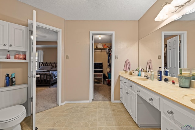ensuite bathroom featuring toilet, a sink, a textured ceiling, tile patterned flooring, and double vanity