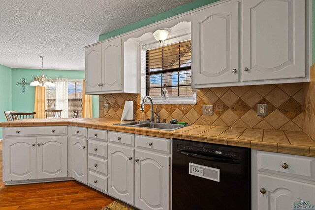 kitchen with black dishwasher, a peninsula, wood finished floors, white cabinetry, and a sink