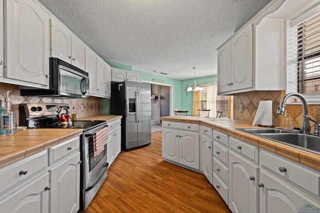 kitchen featuring light wood-type flooring, a peninsula, white cabinets, stainless steel appliances, and a sink