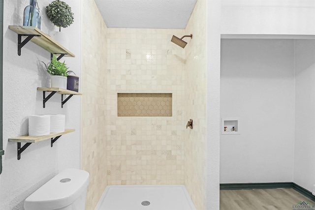 bathroom featuring a tile shower, wood-type flooring, a textured ceiling, and toilet