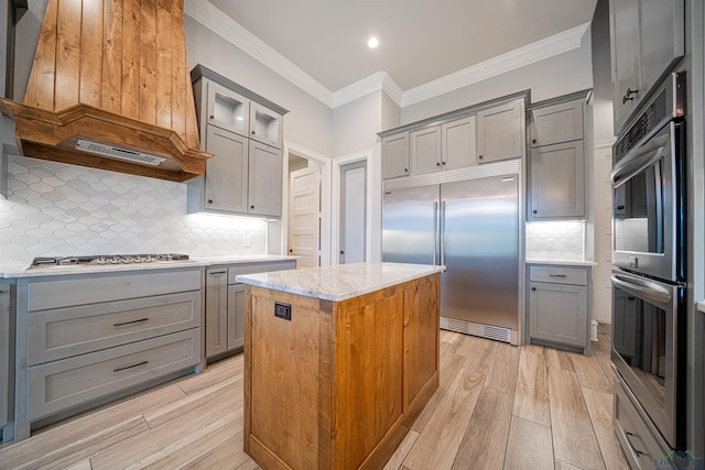 kitchen featuring light stone countertops, appliances with stainless steel finishes, backsplash, a center island, and light hardwood / wood-style floors