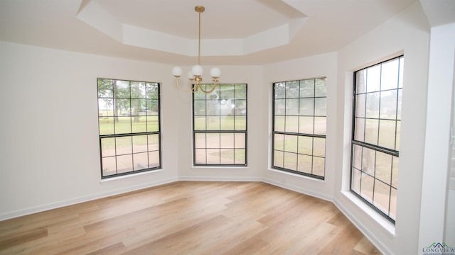 unfurnished dining area featuring light wood-style floors, baseboards, a notable chandelier, and a tray ceiling