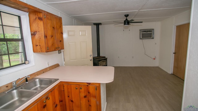 kitchen featuring a wood stove, a peninsula, an AC wall unit, brown cabinets, and a sink