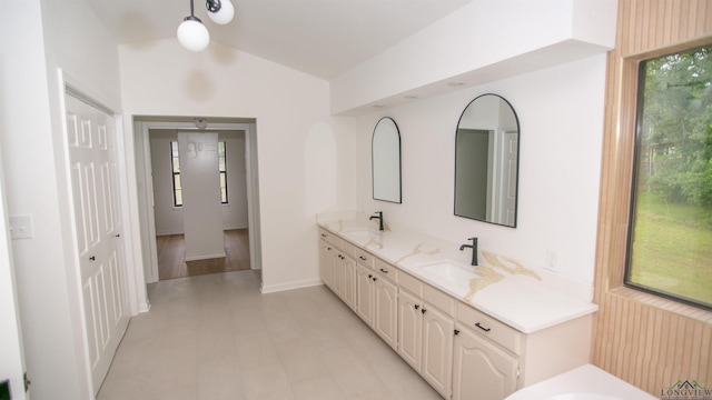 bathroom with a sink, baseboards, double vanity, and lofted ceiling