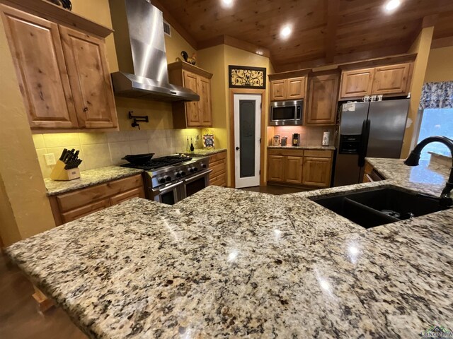 kitchen featuring appliances with stainless steel finishes, tasteful backsplash, wall chimney exhaust hood, wood ceiling, and sink