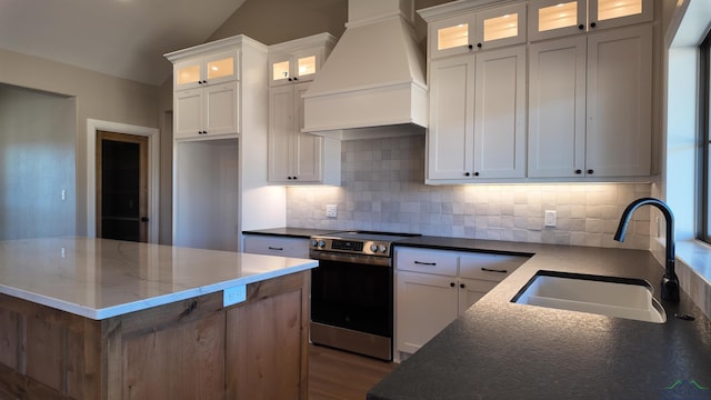 kitchen featuring electric stove, custom range hood, a sink, and white cabinets