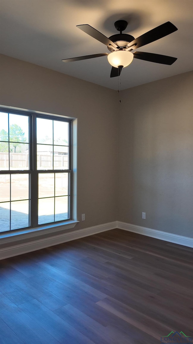 spare room with a healthy amount of sunlight, ceiling fan, baseboards, and dark wood finished floors