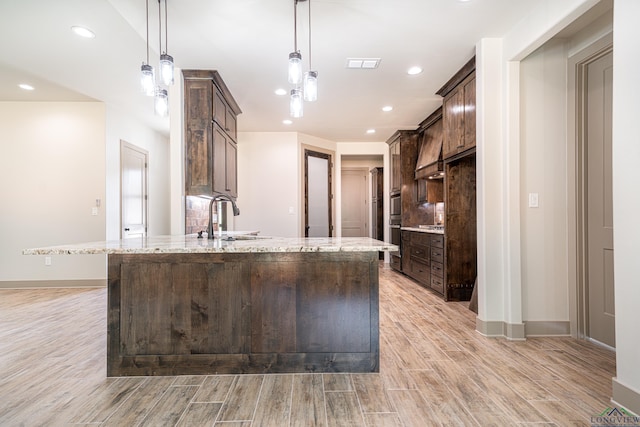 kitchen with sink, light stone countertops, double oven, decorative light fixtures, and dark brown cabinetry