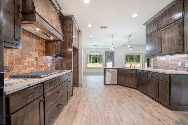 kitchen featuring dark brown cabinetry, stainless steel appliances, premium range hood, backsplash, and decorative light fixtures