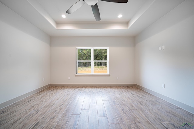 empty room with a raised ceiling, ceiling fan, and light wood-type flooring