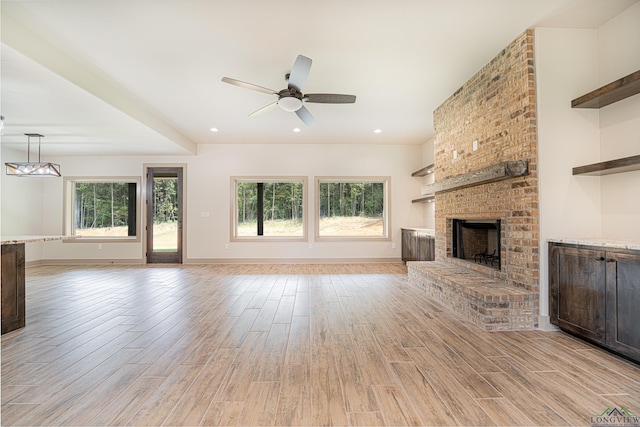 unfurnished living room with a wealth of natural light, a fireplace, ceiling fan, and light wood-type flooring